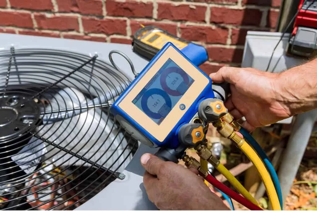 Professional HVAC technician testing air conditioning system with digital manifold gauge.