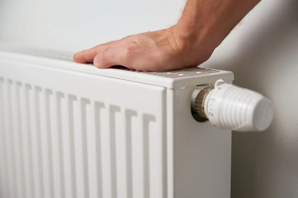 Close-up of a hand adjusting a radiator thermostat for home heating.